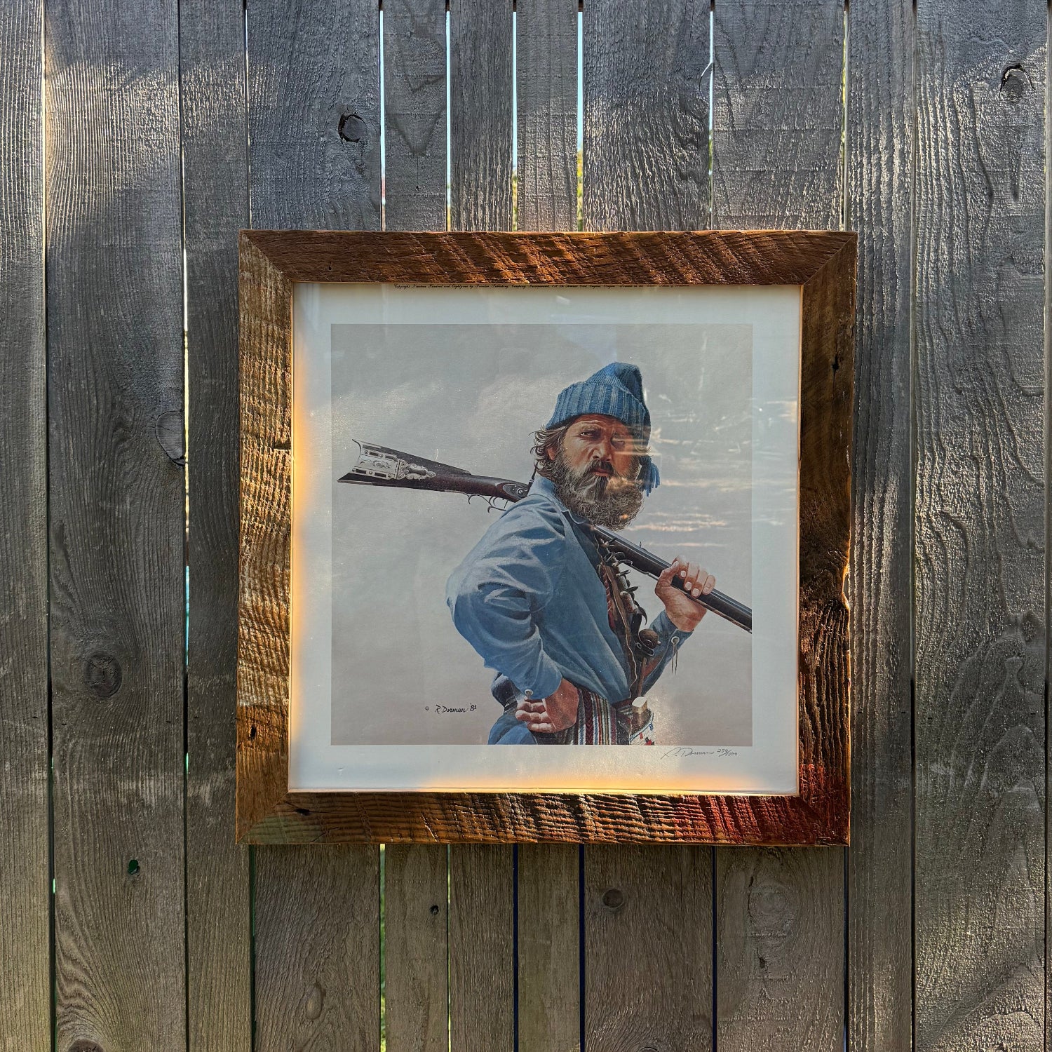 Framed portrait of a person holding a rifle on a wooden wall.