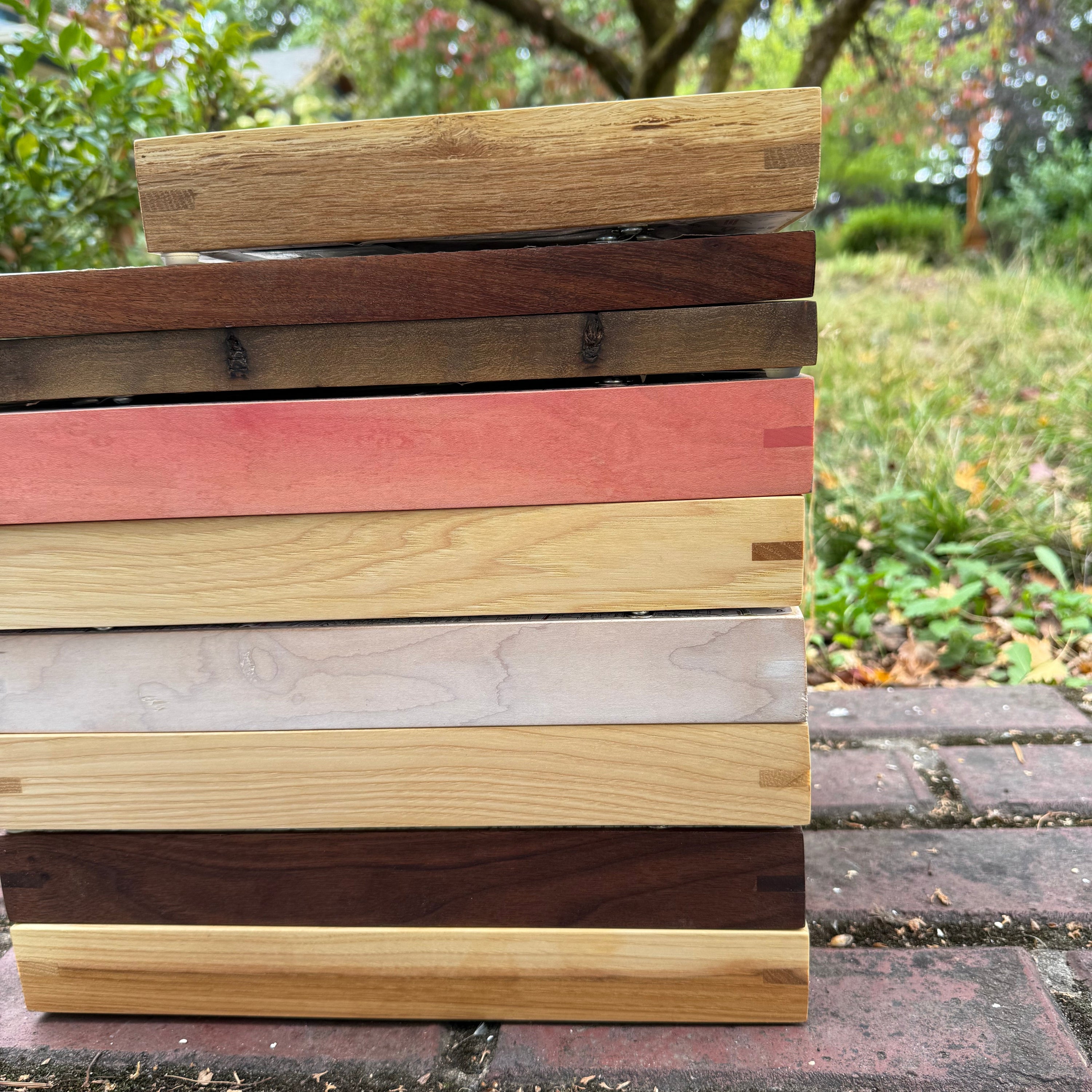 Set of wooden slats in various colors against a brick wall with greenery in the background