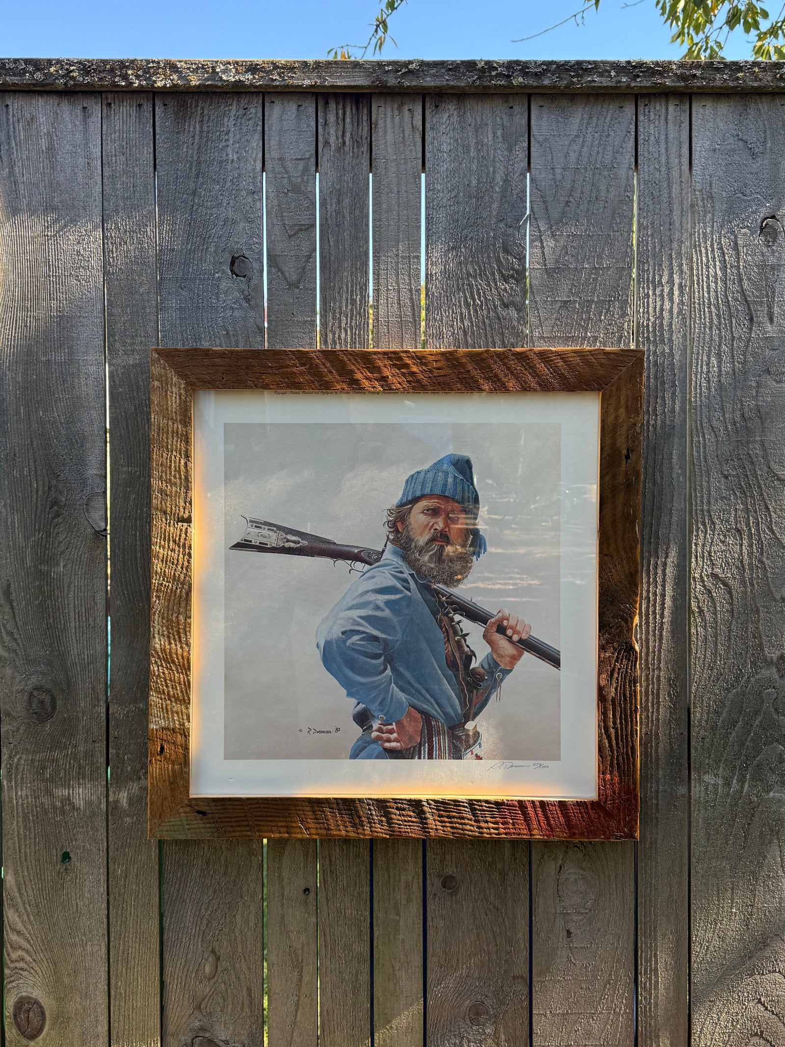 Framed portrait of a person holding a rifle on a wooden wall.